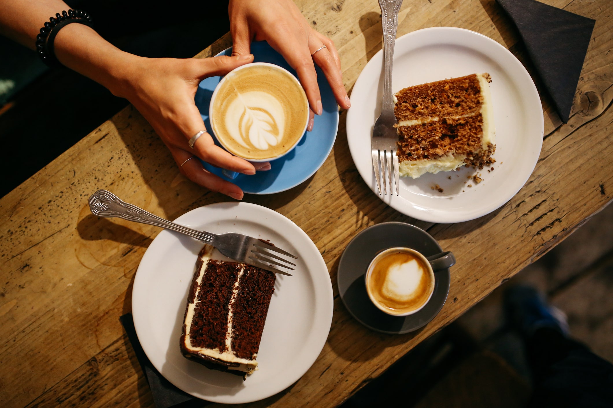woman holding cup of coffeee next to 2 slices of cake on plates